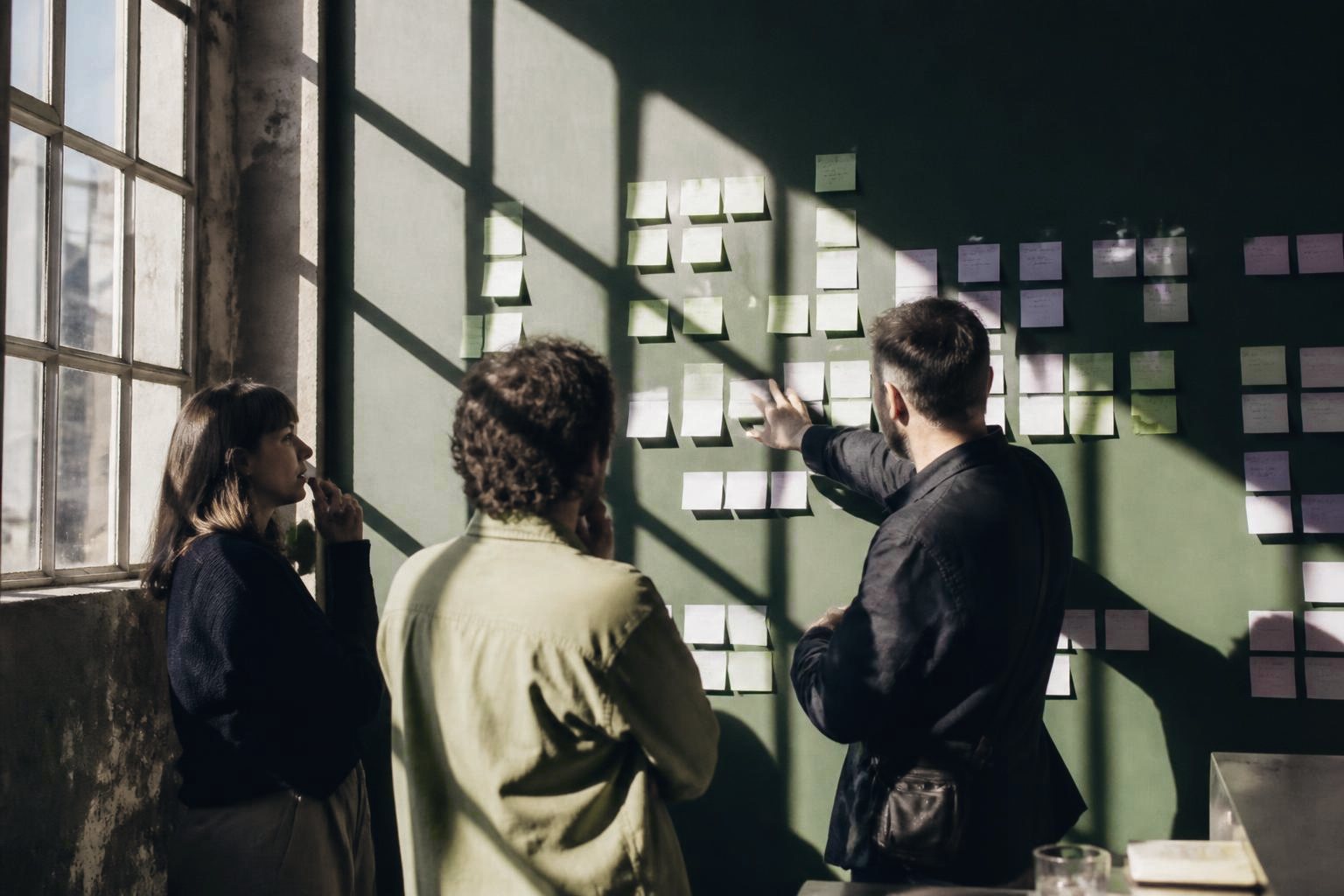 Drei Menschen ordnen Notizen an einer grünen Wand im Gegenlicht